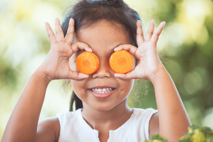 Child holding carrots of her eyes