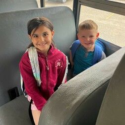 Two kids smiling and sitting on their seats