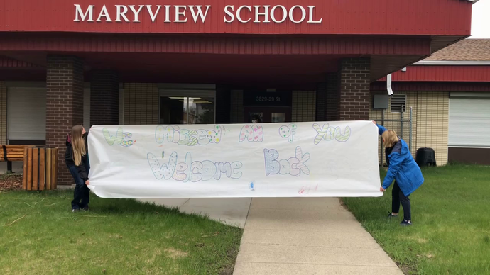 Students running and breaking a banner that says we miss you